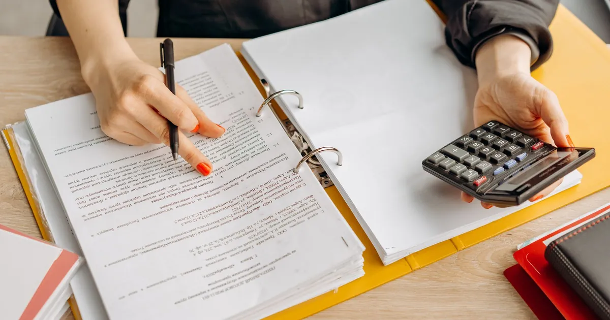 Person comparing out-of-pocket costs in a plan binder with a calculator on a desk