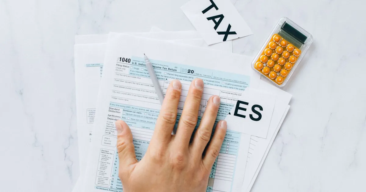 Person completing tax forms with a calculator on a desk