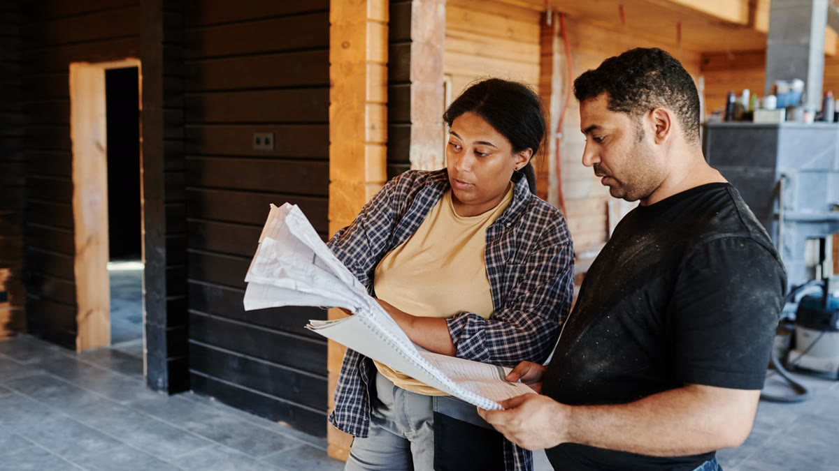 Two construction professionals in hard hats reviewing building plans inside an active project