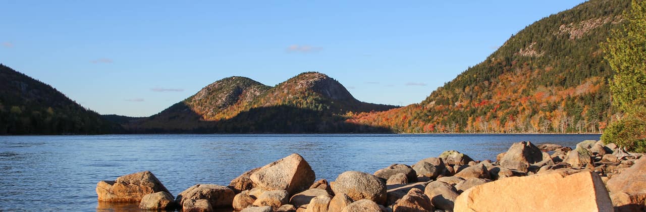 Jordan Pond in Acadia National Park, Maine, with the rounded Bubbles mountains and autumn foliage behind pink granite boulders
