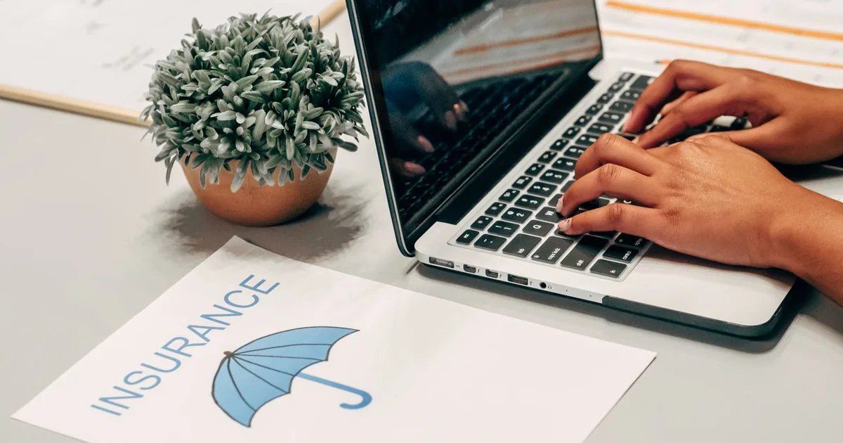 Hands typing on a laptop next to an insurance form on a desk, representing an employer reviewing health insurance renewal options